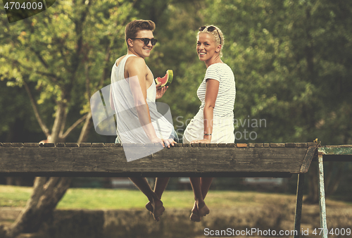 Image of couple enjoying watermelon while sitting on the wooden bridge