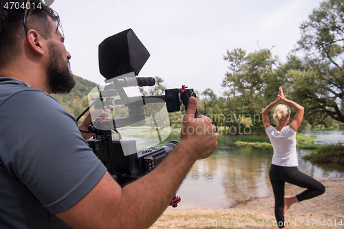 Image of young videographer recording while woman doing yoga exercise