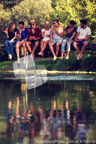 Image of friends enjoying watermelon while sitting on the wooden bridge