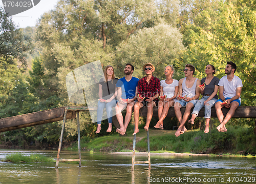 Image of friends enjoying watermelon while sitting on the wooden bridge