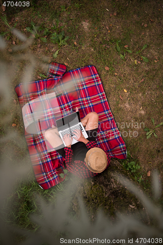 Image of top view of man using a laptop computer under the tree