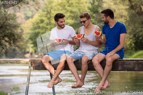 Image of men enjoying watermelon while sitting on the wooden bridge