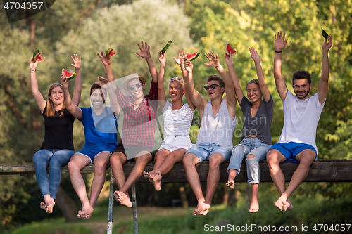 Image of friends enjoying watermelon while sitting on the wooden bridge