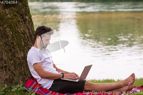 Image of man using a laptop computer on the bank of the river