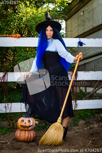 Image of Cute girl in a witch costume with pumpkins and a broom