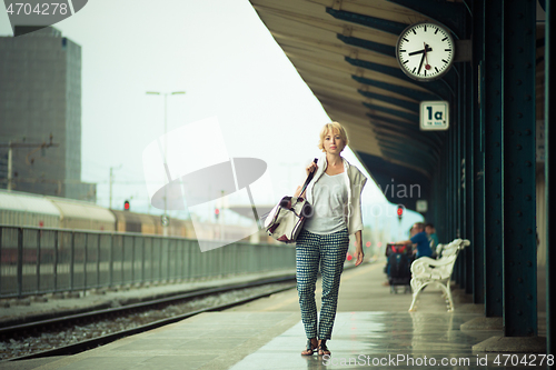 Image of Blonde caucasian woman waiting at the railway station carrying bag