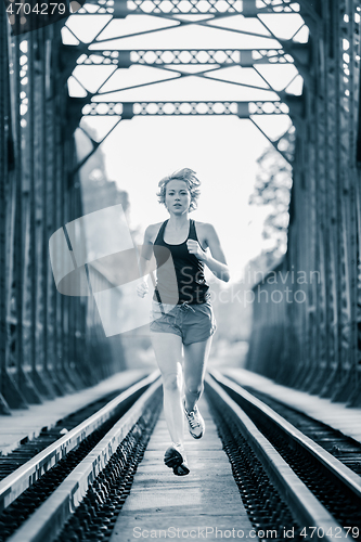 Image of Athlete running on railaway bridge training for marathon and fitness. Healthy sporty caucasian woman exercising in urban environment before going to work. Active urban lifestyle