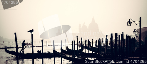 Image of Romantic Italian city of Venice, a World Heritage Site: traditional Venetian wooden boats, gondolier and Roman Catholic church Basilica di Santa Maria della Salute in the misty background