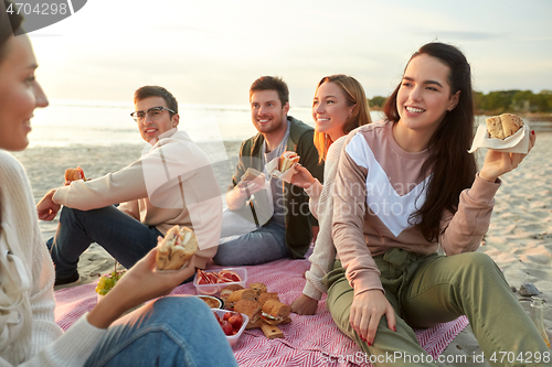 Image of happy friends eating sandwiches at picnic on beach