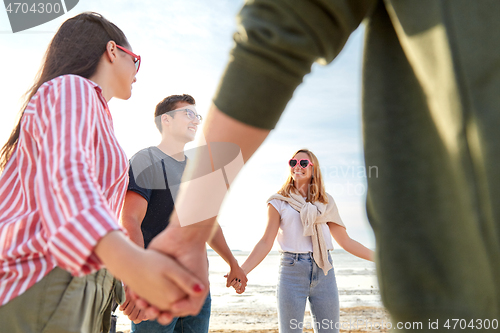 Image of happy friends holding hands on summer beach