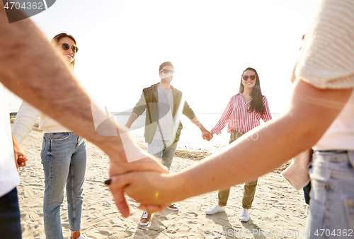 Image of happy friends holding hands on summer beach