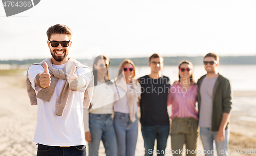 Image of happy man with friends on beach showing thumbs up