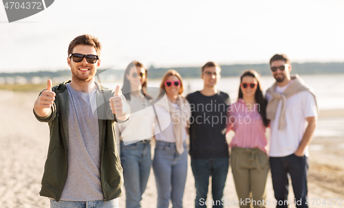 Image of happy man with friends on beach showing thumbs up