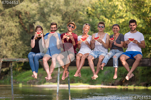 Image of friends enjoying watermelon while sitting on the wooden bridge