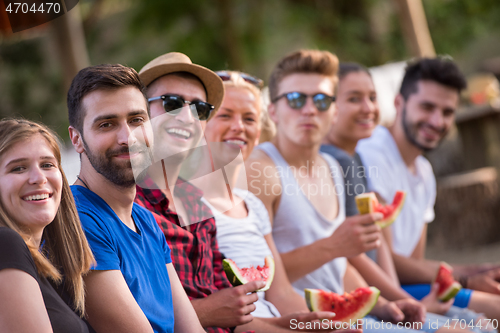 Image of friends enjoying watermelon while sitting on the wooden bridge