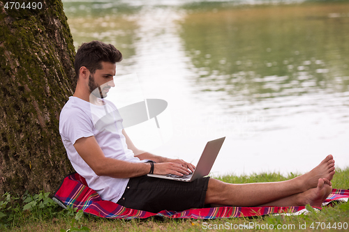 Image of man using a laptop computer on the bank of the river