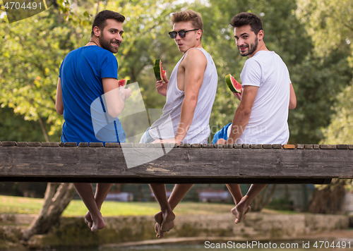 Image of men enjoying watermelon while sitting on the wooden bridge