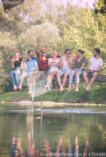 Image of friends enjoying watermelon while sitting on the wooden bridge