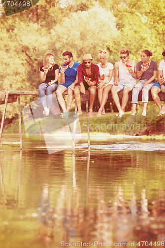 Image of friends enjoying watermelon while sitting on the wooden bridge