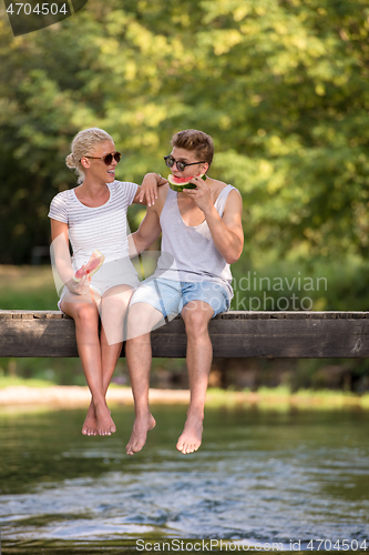 Image of couple enjoying watermelon while sitting on the wooden bridge