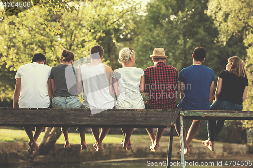 Image of rear view of friends enjoying watermelon while sitting on the wo