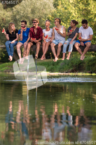 Image of friends enjoying watermelon while sitting on the wooden bridge