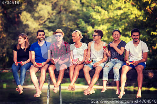 Image of friends enjoying watermelon while sitting on the wooden bridge