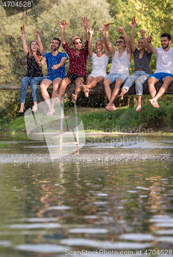 Image of friends enjoying watermelon while sitting on the wooden bridge