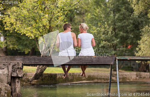 Image of couple enjoying watermelon while sitting on the wooden bridge