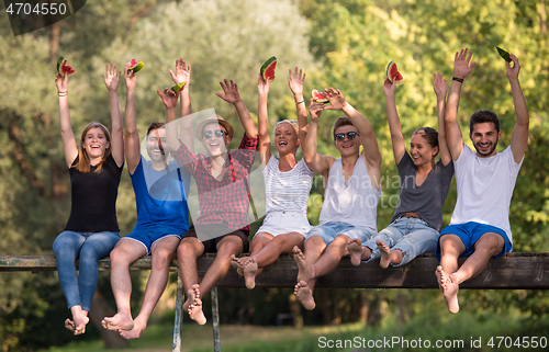 Image of friends enjoying watermelon while sitting on the wooden bridge