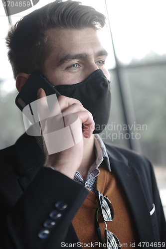 Image of business man wearing coronavirus medical face mask while using smartphone