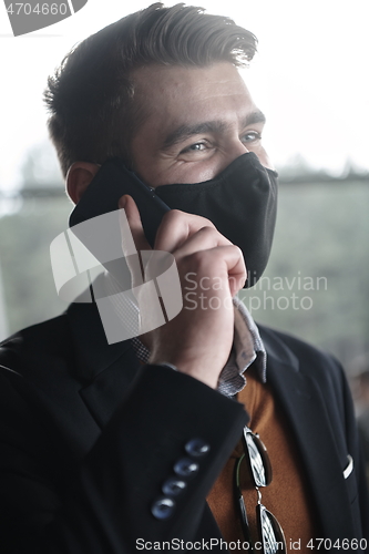 Image of business man wearing coronavirus medical face mask while using smartphone