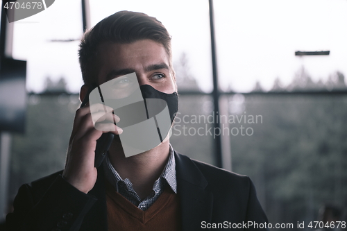 Image of business man wearing coronavirus medical face mask while using smartphone