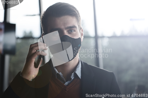 Image of business man wearing coronavirus medical face mask while using smartphone