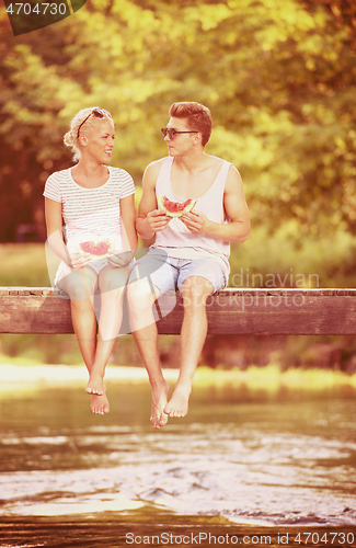 Image of couple enjoying watermelon while sitting on the wooden bridge