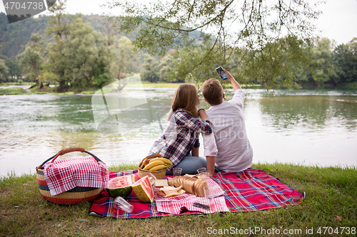 Image of Couple taking a selfie by mobile phone while enjoying picnic tim