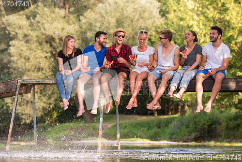 Image of friends enjoying watermelon while sitting on the wooden bridge