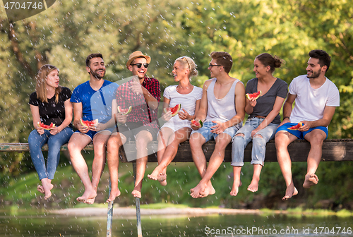 Image of friends enjoying watermelon while sitting on the wooden bridge