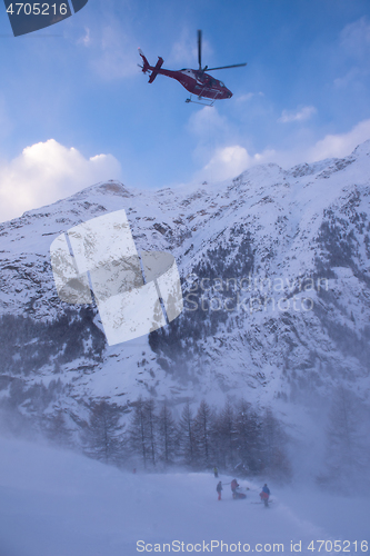 Image of rescue team with a red helicopter rescuing a hurt skier