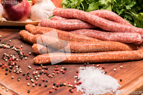 Image of raw sausages with chilli and herbs on a wooden board with spices