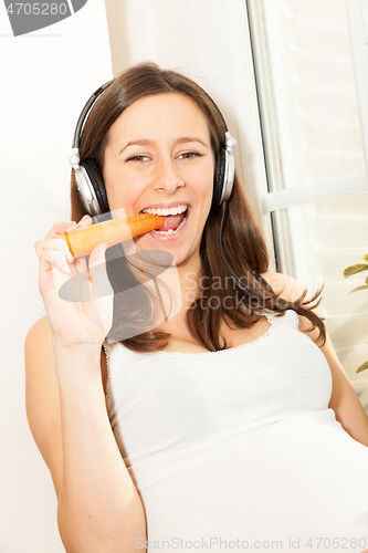 Image of pregnant woman eat a carrot and listening to music