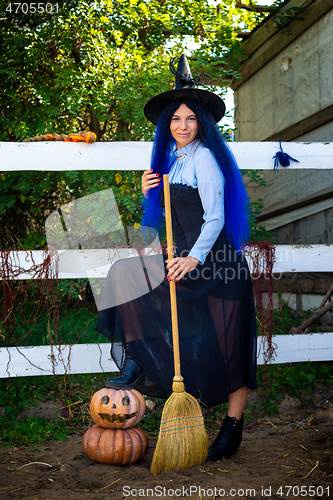 Image of Cute girl in a witch costume with pumpkins and a broom at a Halloween party