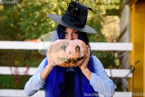 Image of A girl in a witch costume looks out from behind a pumpkin with a painted face