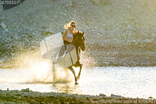 Image of A girl rides a horse in the evening in the water along the river bank