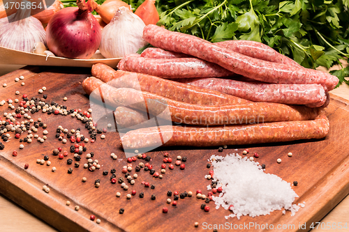 Image of raw sausages with chilli and herbs on a wooden board with spices