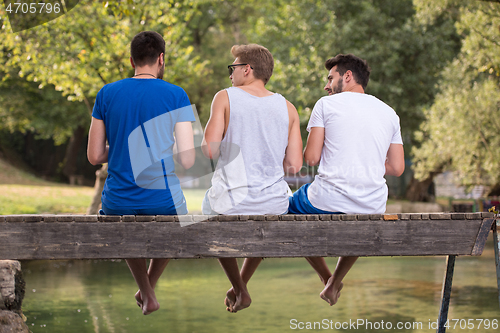 Image of men enjoying watermelon while sitting on the wooden bridge