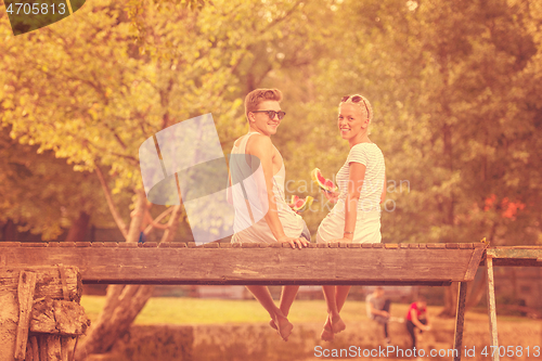 Image of couple enjoying watermelon while sitting on the wooden bridge