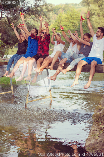 Image of friends enjoying watermelon while sitting on the wooden bridge