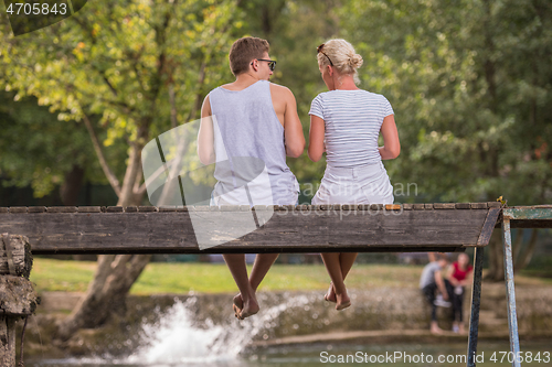 Image of couple enjoying watermelon while sitting on the wooden bridge