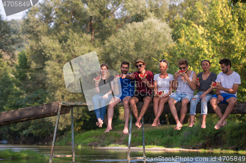 Image of friends enjoying watermelon while sitting on the wooden bridge